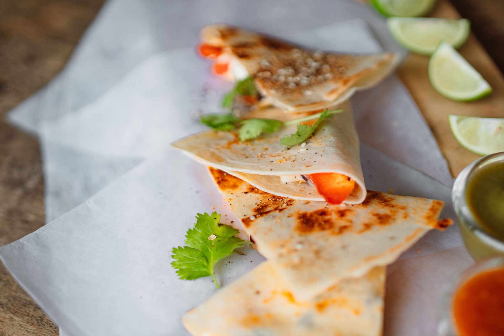 Close-up of a mouth-watering quesadilla with cilantro and lime slices on wax paper.